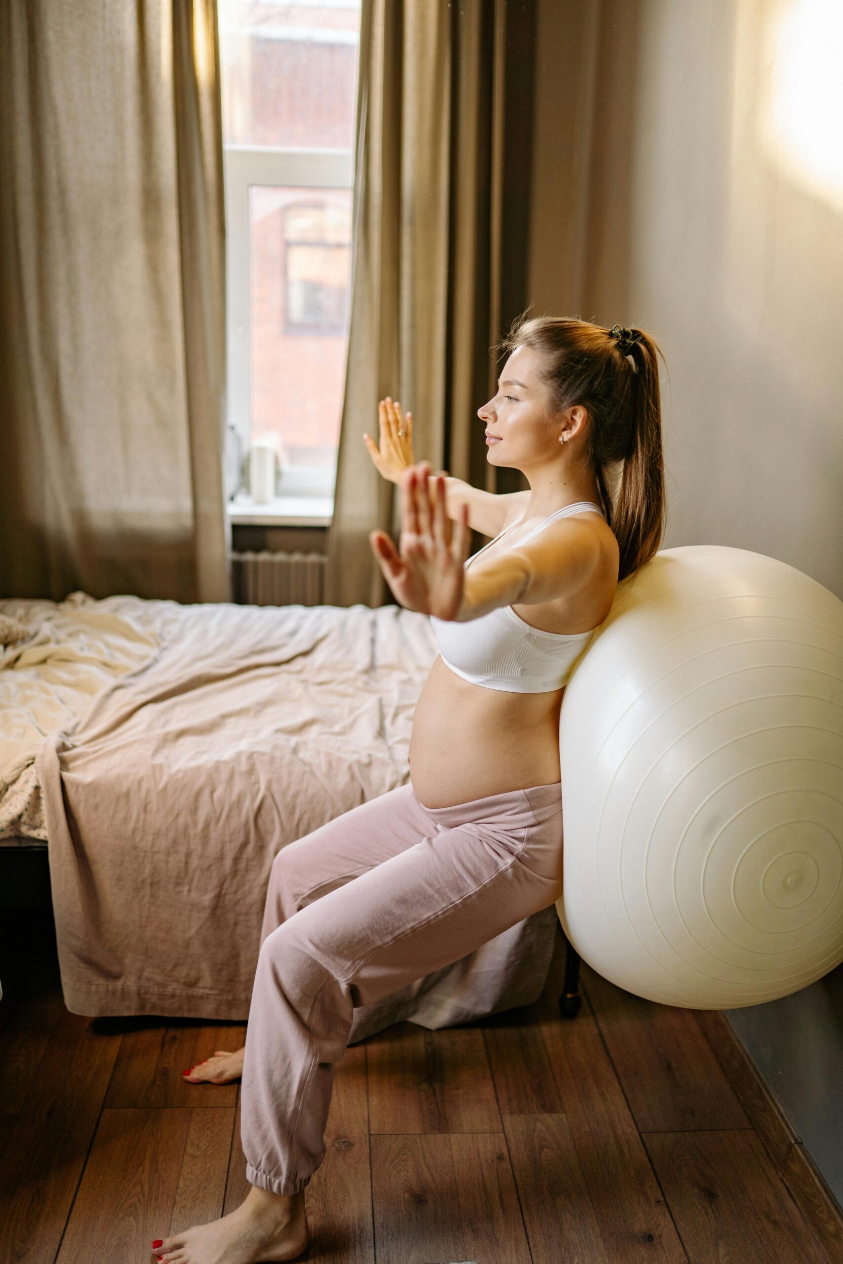 Expectant mother practicing yoga exercises indoors using an exercise ball.